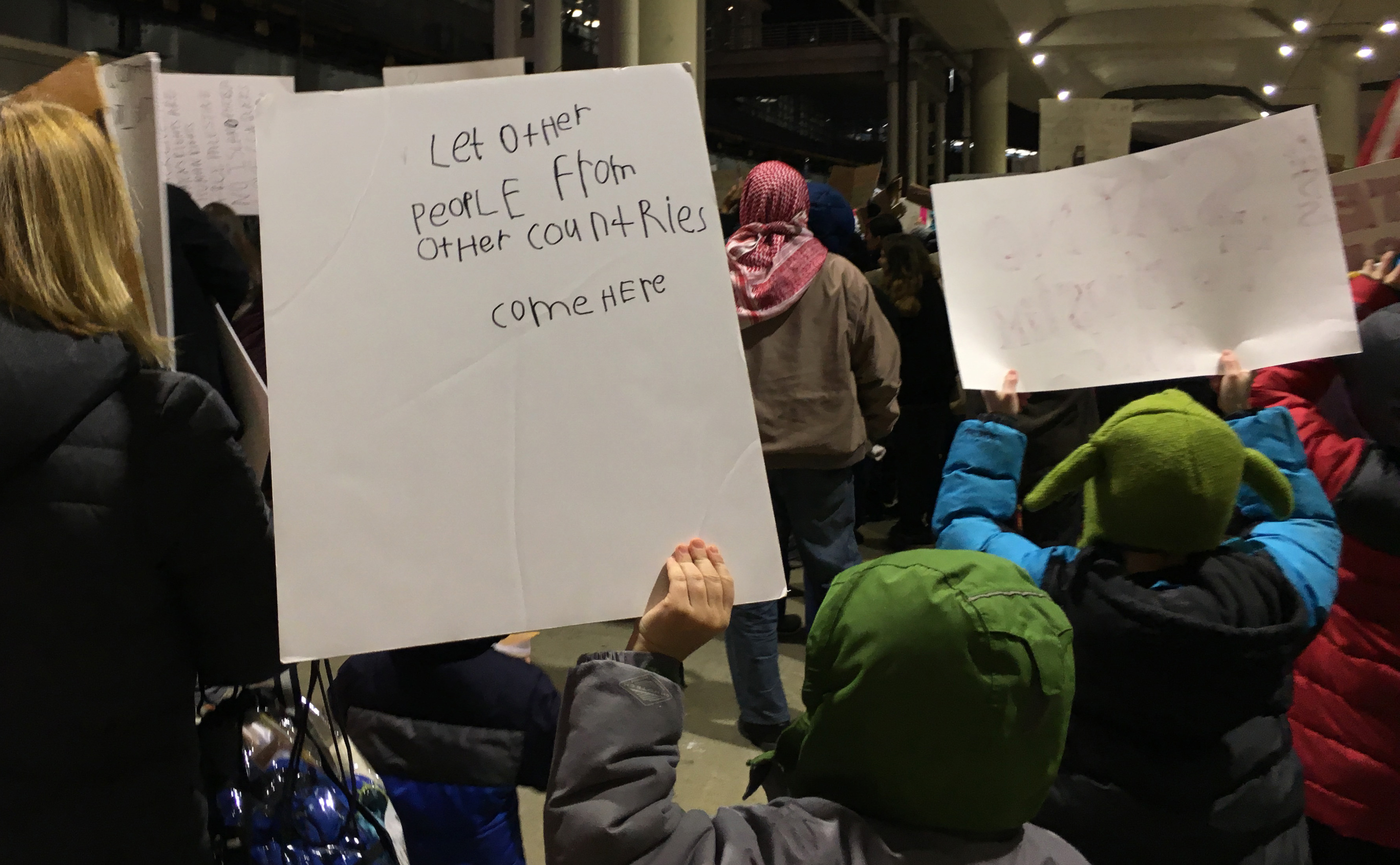 A plea by a youngster among thousands of protesters at Chicago O'Hare International Airport Sunday against President Donald Trump's new immigration policies. (Shen Lu/MEDILL)